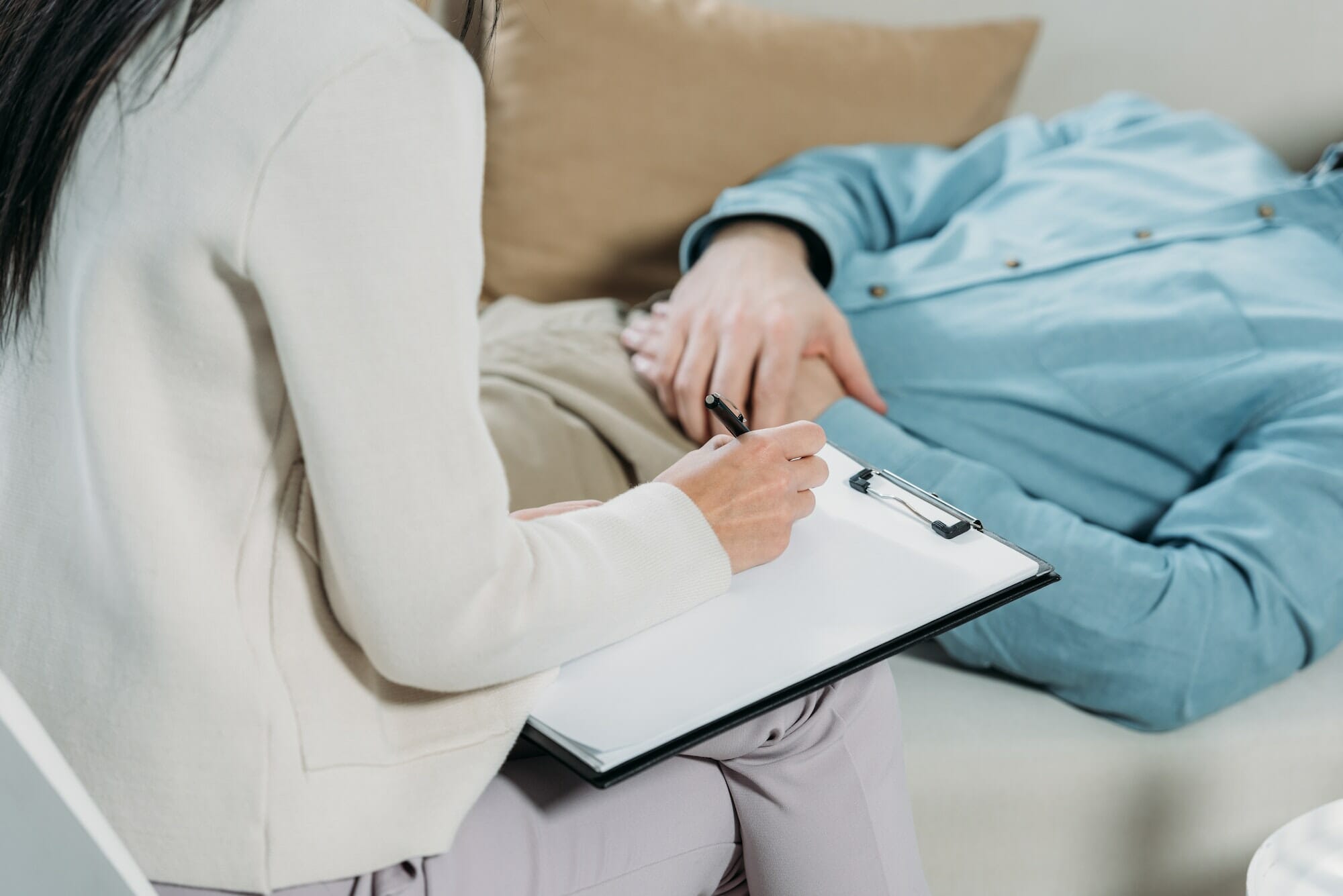 cropped shot of psychotherapist writing on clipboard and male patient lying on couch